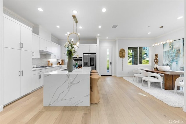 kitchen with stainless steel fridge with ice dispenser, crown molding, gas cooktop, hanging light fixtures, and a kitchen island with sink