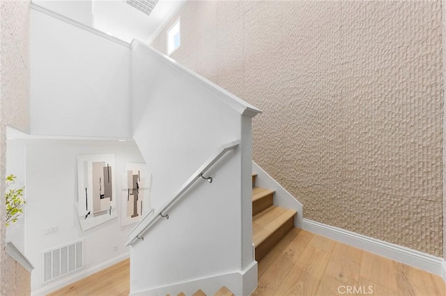 stairs with wood finished floors, a towering ceiling, and baseboards