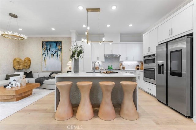 kitchen featuring appliances with stainless steel finishes, a chandelier, a sink, ornamental molding, and under cabinet range hood