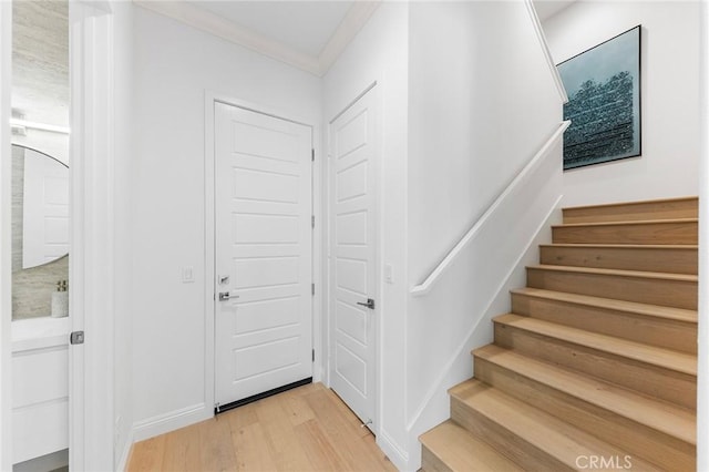 stairs with wood finished floors and ornamental molding
