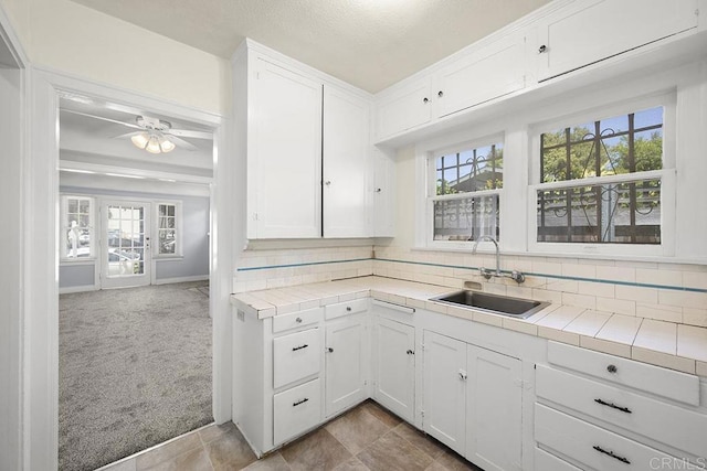 kitchen with a sink, tile counters, plenty of natural light, and white cabinetry