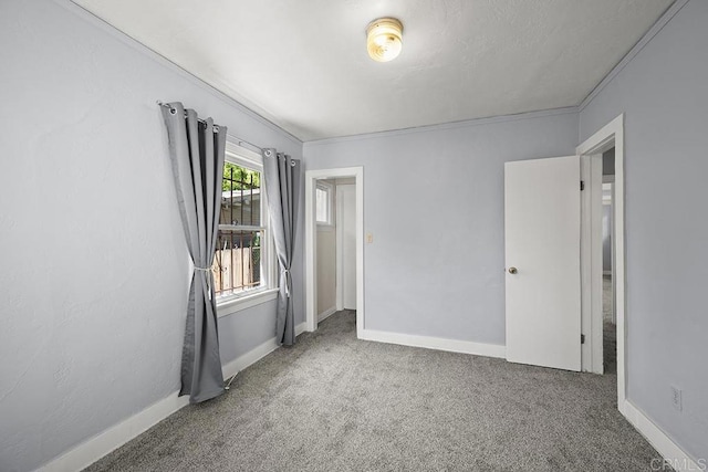 empty room featuring carpet floors, crown molding, and baseboards