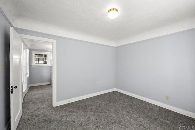 spare room featuring dark carpet and baseboards