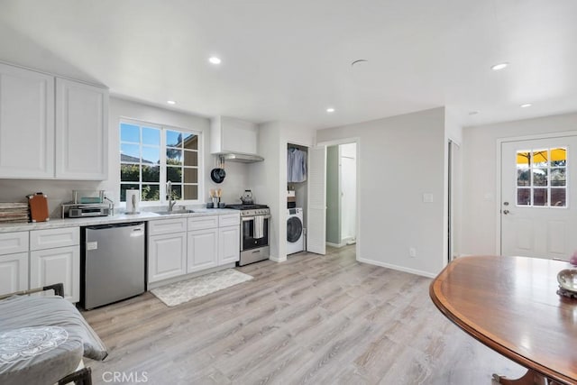 kitchen with stainless steel appliances, washer / dryer, a sink, white cabinets, and light wood finished floors
