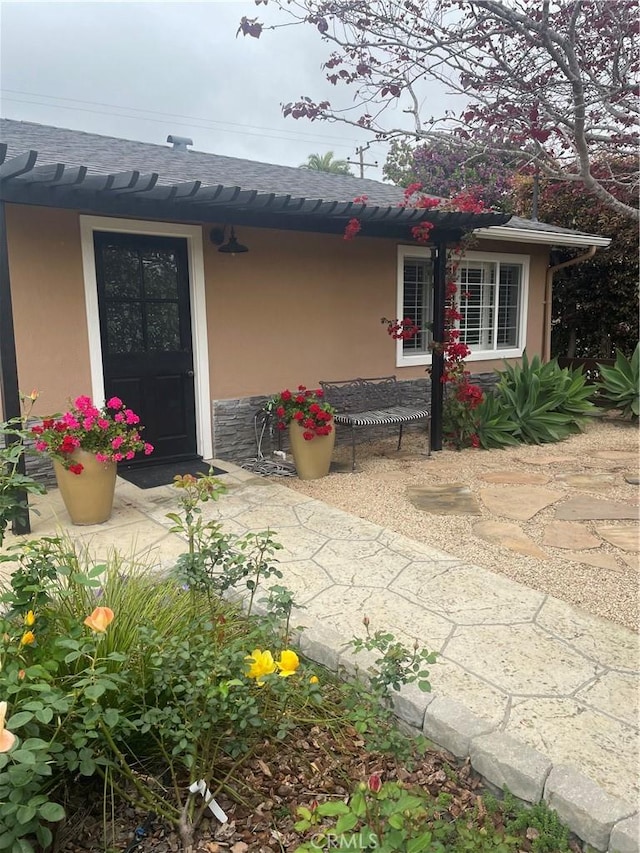 view of exterior entry featuring stucco siding and roof with shingles