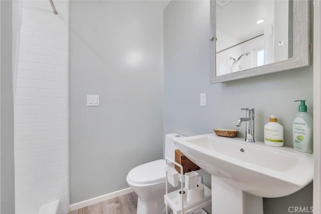 bathroom featuring tiled shower, toilet, wood finished floors, baseboards, and a sink