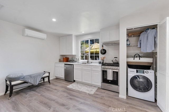 kitchen with washer / dryer, stainless steel appliances, an AC wall unit, a sink, and white cabinets