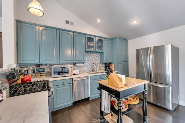 kitchen with stainless steel appliances, a sink, light countertops, vaulted ceiling, and dark wood finished floors