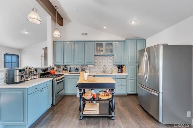 kitchen featuring appliances with stainless steel finishes, a sink, blue cabinetry, decorative backsplash, and dark wood finished floors