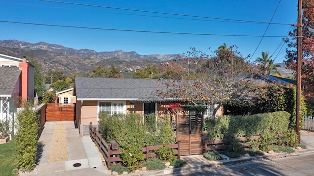 view of front facade with fence, a mountain view, roof with shingles, and stucco siding