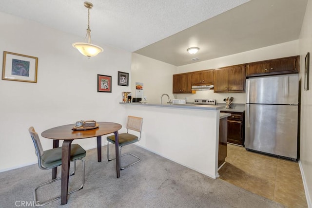 kitchen featuring freestanding refrigerator, under cabinet range hood, light countertops, pendant lighting, and a peninsula