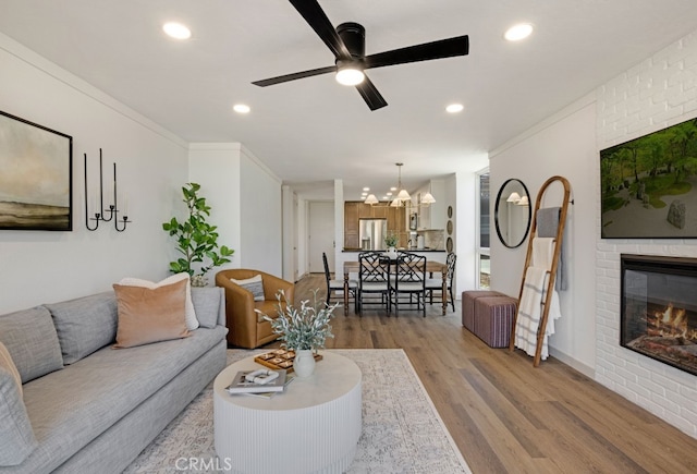 living area with wood finished floors, recessed lighting, a brick fireplace, a ceiling fan, and a chandelier
