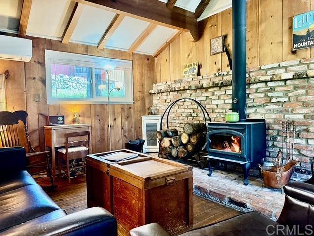 22104 Crestline, Palomar Mountain, CA 92060 - living area with a wood stove, wood-type flooring, wood walls, and a wall unit AC
