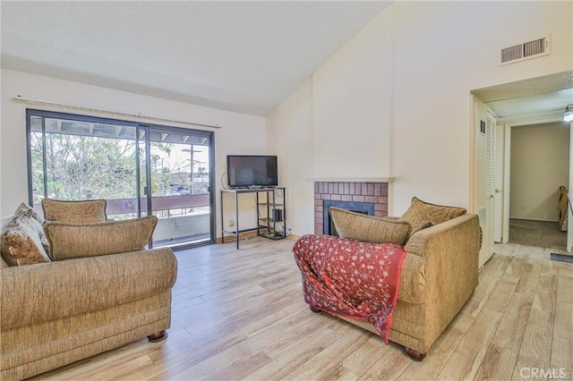 living room featuring high vaulted ceiling, light wood finished floors, and a brick fireplace