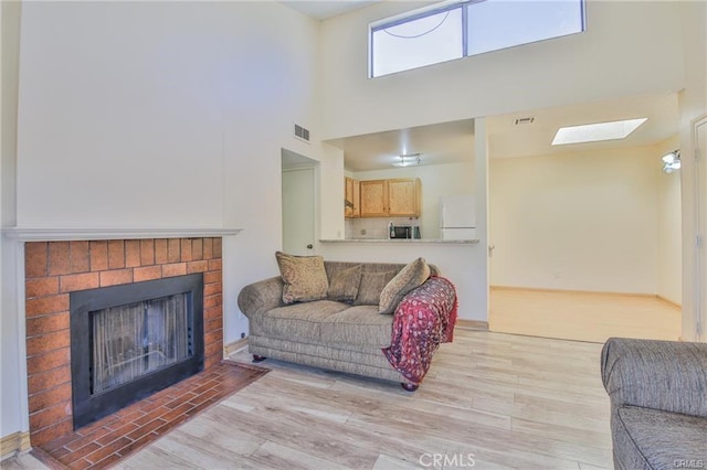 living room with a high ceiling, a fireplace, light wood-style floors, and a skylight