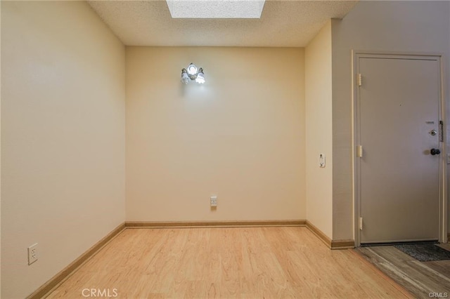 empty room with light wood-style flooring, a skylight, baseboards, and a textured ceiling
