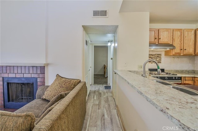 kitchen with under cabinet range hood, light wood-style floors, light countertops, decorative backsplash, and a fireplace