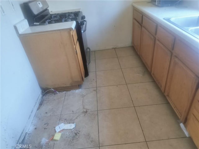kitchen with gas stove, baseboards, a sink, light tile patterned floors, and light countertops