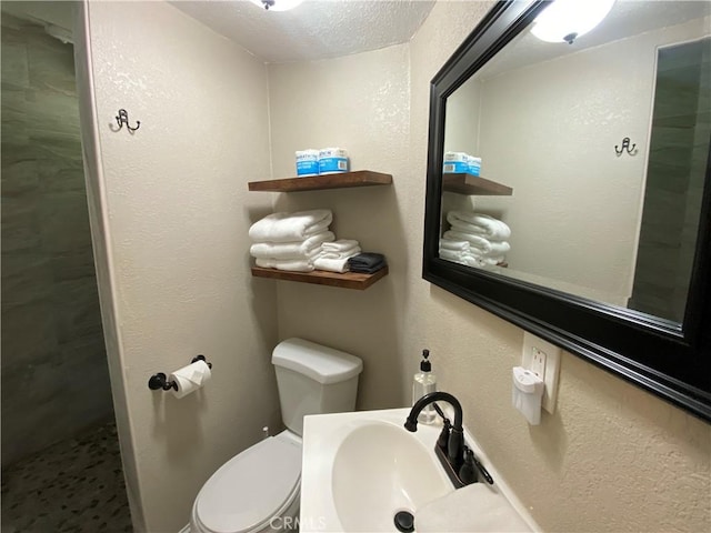 full bathroom with a sink, a textured ceiling, toilet, and a tile shower