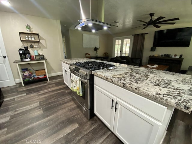 kitchen featuring stainless steel gas stove, wall chimney exhaust hood, a ceiling fan, and dark wood finished floors