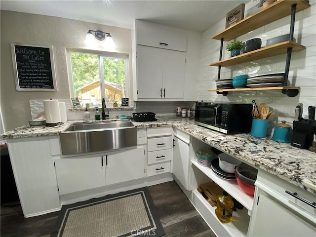kitchen with a sink, open shelves, dark wood-style flooring, white cabinets, and light stone countertops