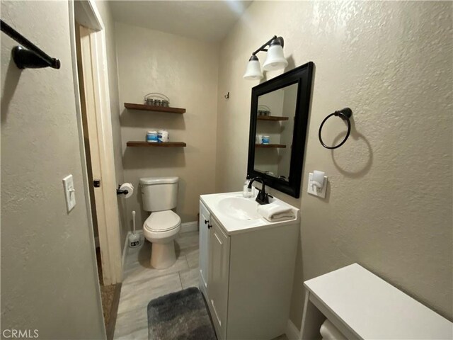 bathroom with toilet, vanity, tile patterned flooring, a textured wall, and baseboards