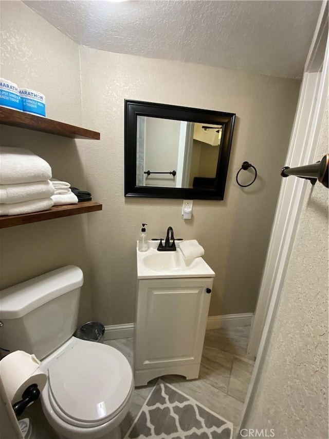 half bath with baseboards, toilet, vanity, and a textured ceiling