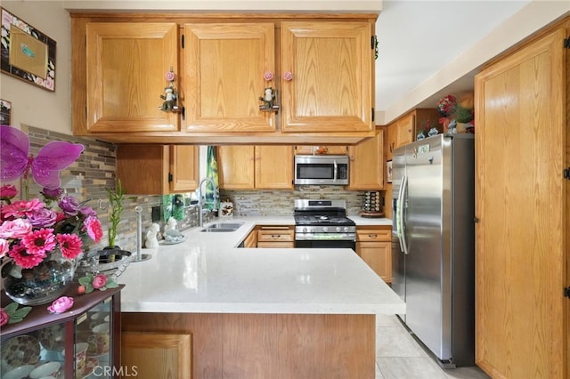 kitchen featuring appliances with stainless steel finishes, a sink, light countertops, a peninsula, and backsplash
