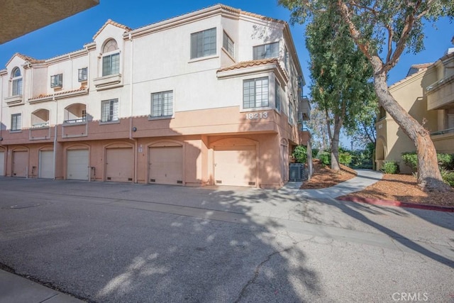 18213 Flynn Dr Unit 132, Canyon Country, CA 91387 - view of front facade with stucco siding, a tile roof, an attached garage, driveway, and cooling unit