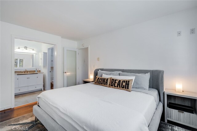 bedroom featuring a sink, ensuite bath, and wood finished floors