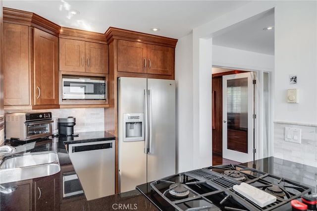 kitchen featuring appliances with stainless steel finishes, backsplash, brown cabinetry, dark stone countertops, and a sink