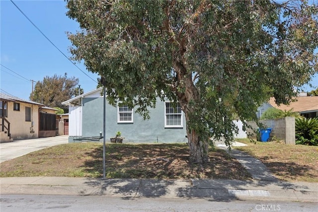 view of property hidden behind natural elements with stucco siding, driveway, and fence
