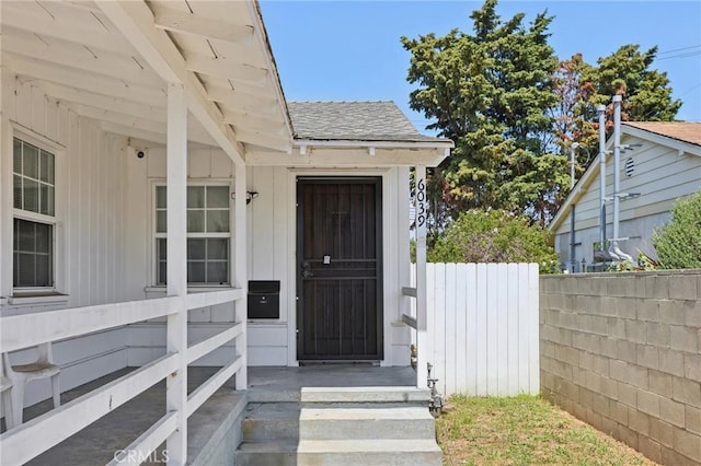 property entrance with fence, roof with shingles, and board and batten siding