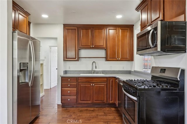kitchen featuring stainless steel appliances, a sink, dark wood-style floors, recessed lighting, and brown cabinetry