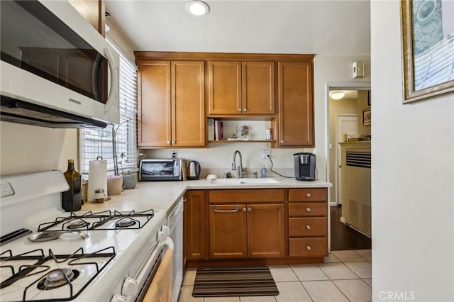 kitchen featuring white appliances, a sink, light countertops, light tile patterned floors, and brown cabinetry