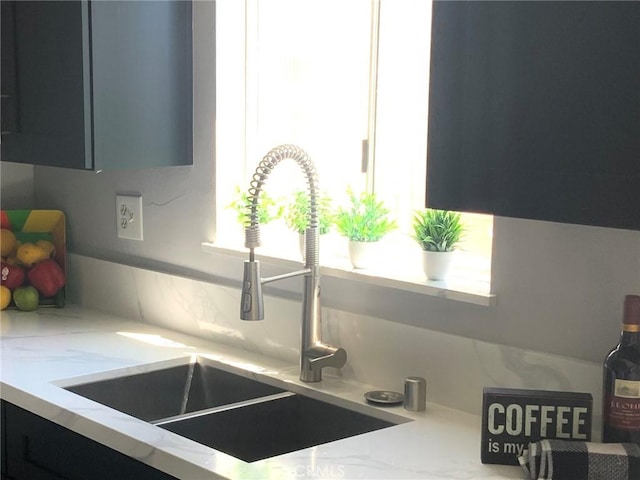 kitchen view of a sink, light stone countertops, and dark cabinetry