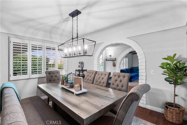 dining area with wood finished floors, a chandelier, arched walkways, and baseboards