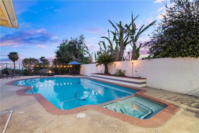 pool at dusk with a patio, a fenced backyard, and a pool with connected hot tub