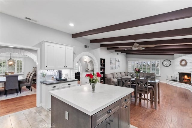 kitchen featuring open floor plan, a brick fireplace, white cabinetry, ceiling fan, and beam ceiling