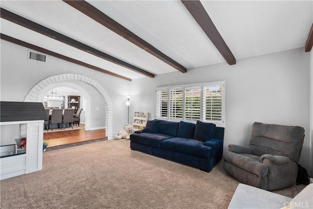 carpeted living room featuring beamed ceiling, arched walkways, and a chandelier