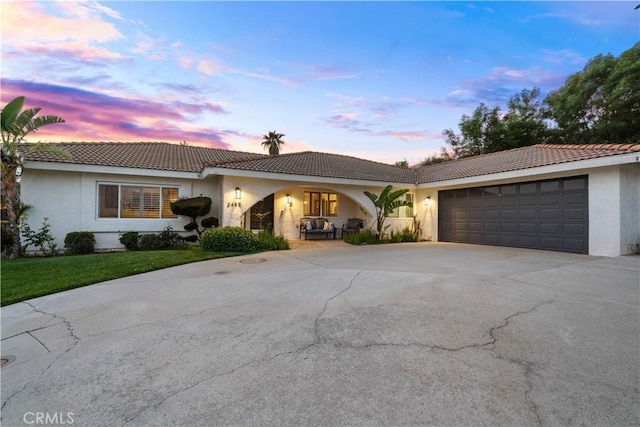 ranch-style house with driveway, stucco siding, a garage, a tile roof, and a yard