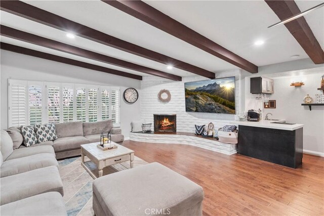 living area featuring beam ceiling, baseboards, light wood-style flooring, a brick fireplace, and recessed lighting