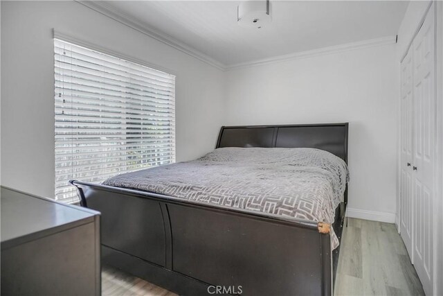 bedroom with light wood-type flooring, ornamental molding, a closet, and baseboards