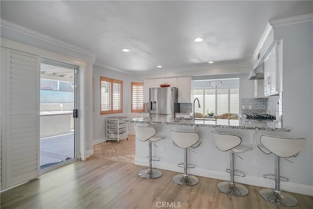 kitchen featuring stainless steel appliances, crown molding, a peninsula, decorative backsplash, and white cabinets