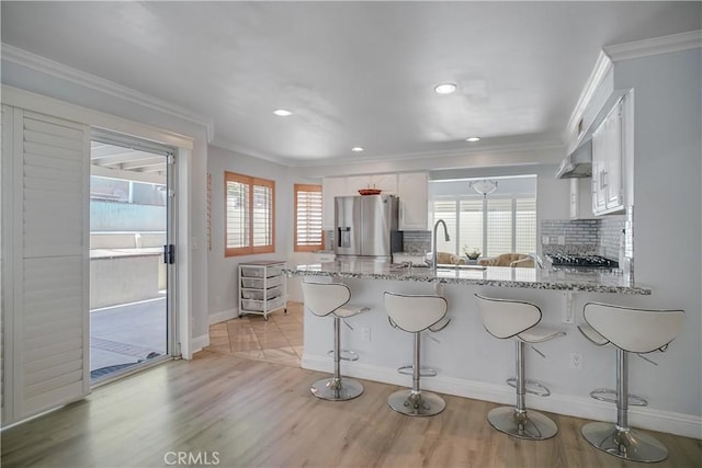 kitchen featuring stainless steel appliances, crown molding, a peninsula, decorative backsplash, and white cabinetry