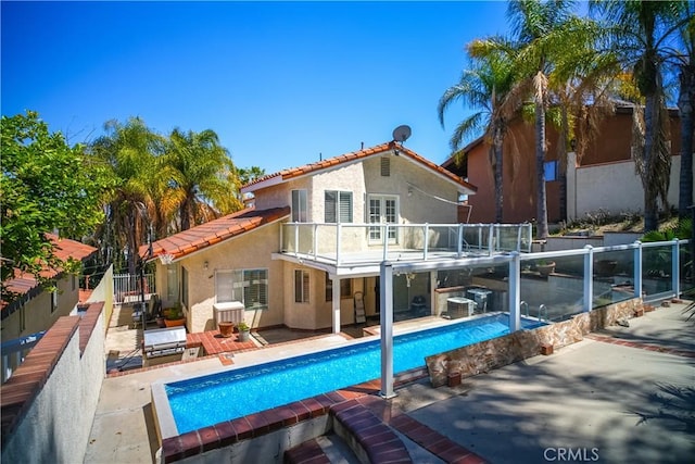 rear view of house featuring stucco siding, a patio, a tile roof, a balcony, and fence