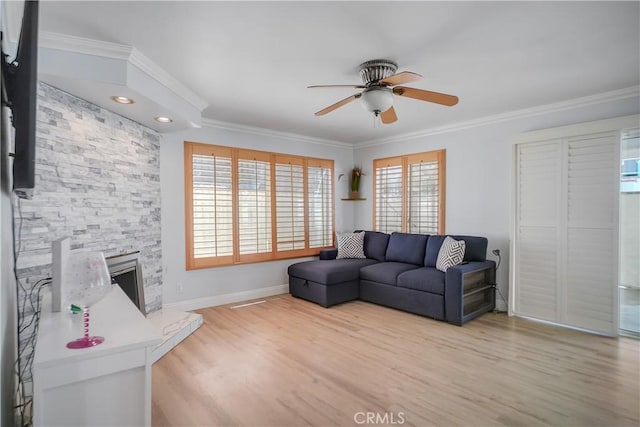 living room with a ceiling fan, light wood-style floors, crown molding, baseboards, and a stone fireplace