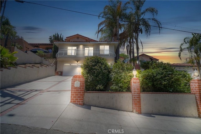 mediterranean / spanish-style house with a balcony, concrete driveway, a garage, stucco siding, and fence