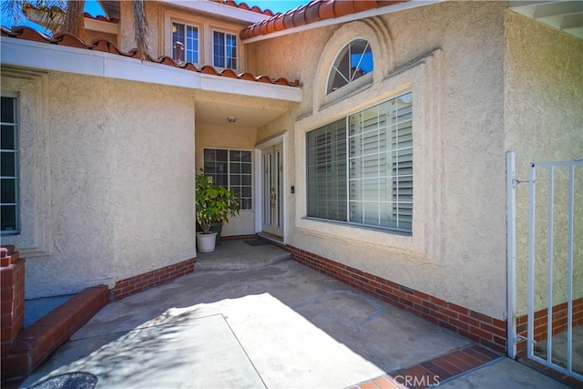 view of exterior entry with stucco siding, a patio, and a tiled roof