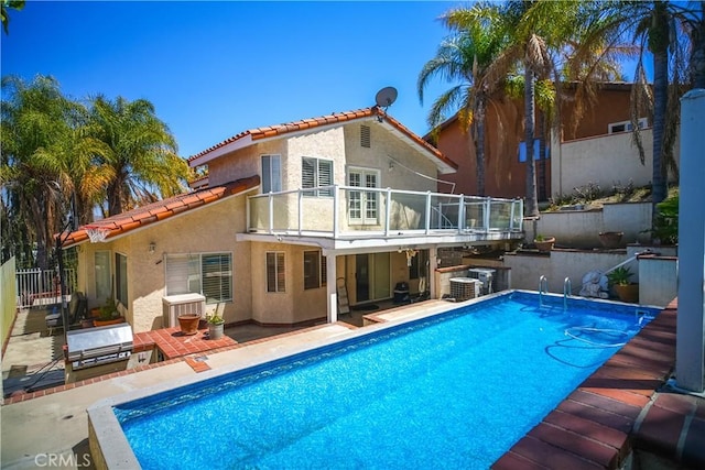 rear view of house with a balcony, a tile roof, stucco siding, fence, and a patio